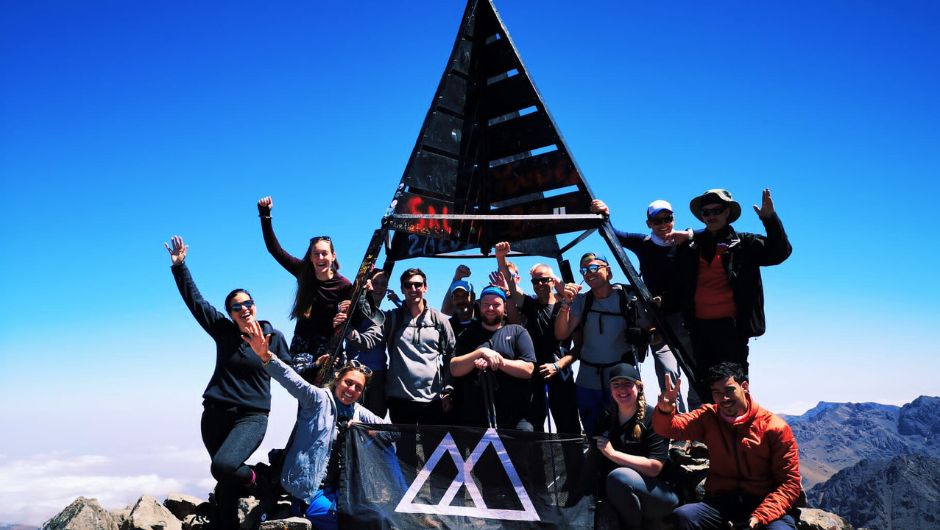 Charity Challenge Trekkers celebrating in front of the sign on the summit of Mt Toubkal in Morocco with clear blue skies