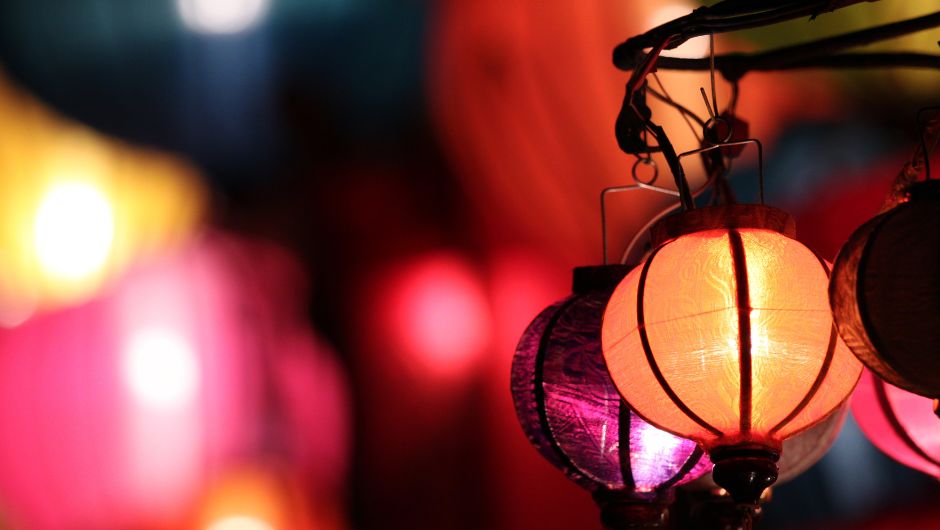 Colourful paper lanterns glowing to the right hand side of image, the rest of the image is out of focus. 