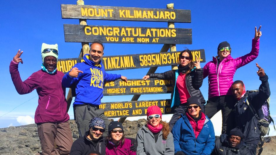 A group of trekkers standing in front of the Mt Kilimanjaro summit sign, Tanzania