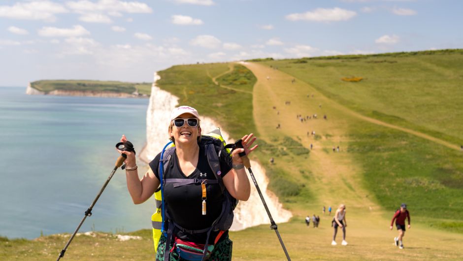 A walker with walking poles on the Sevens Sister, South Downs Way on a clear day with blue skies
