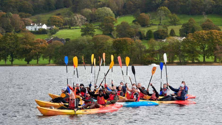 A group of kayakers  with oars in the air on Coniston water in the Lake District

