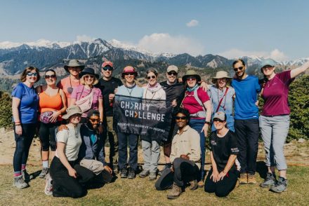 a group of smiling challengers posing with a Charity Challenge flag, surrounded by Indian Himalaya mountains