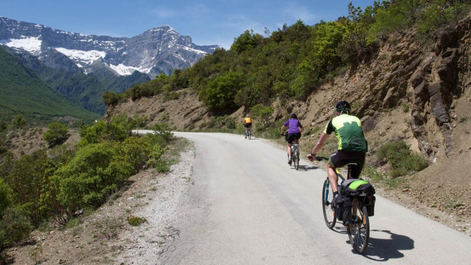 Three cyclists riding along a road, with mountain scenery in the background.