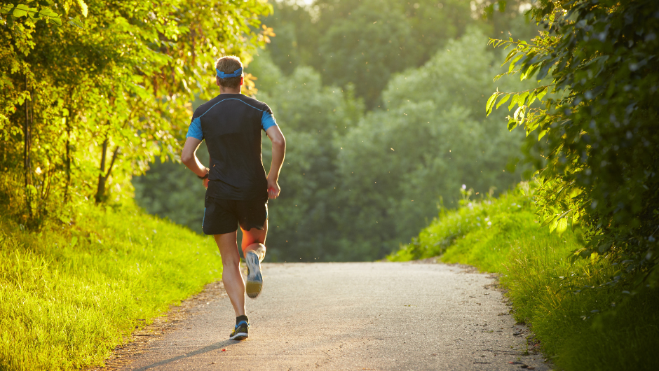 A man jogging on pavement surrounded by grass and trees.