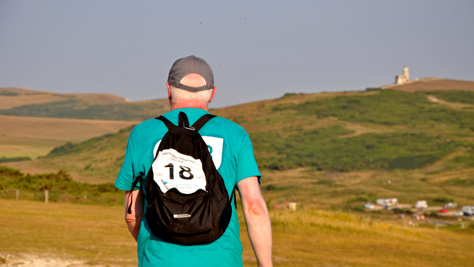 A solo trekker wearing a backpack, cap and Charity Challenge number trekking over vast green fields.