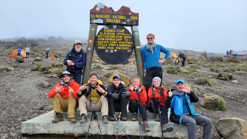 A group of challengers posing in front of a Kilimanjaro National Park camp sign in Tanzania.