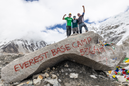 Three people stood cheering on a rock that's signed Everest Base Camp