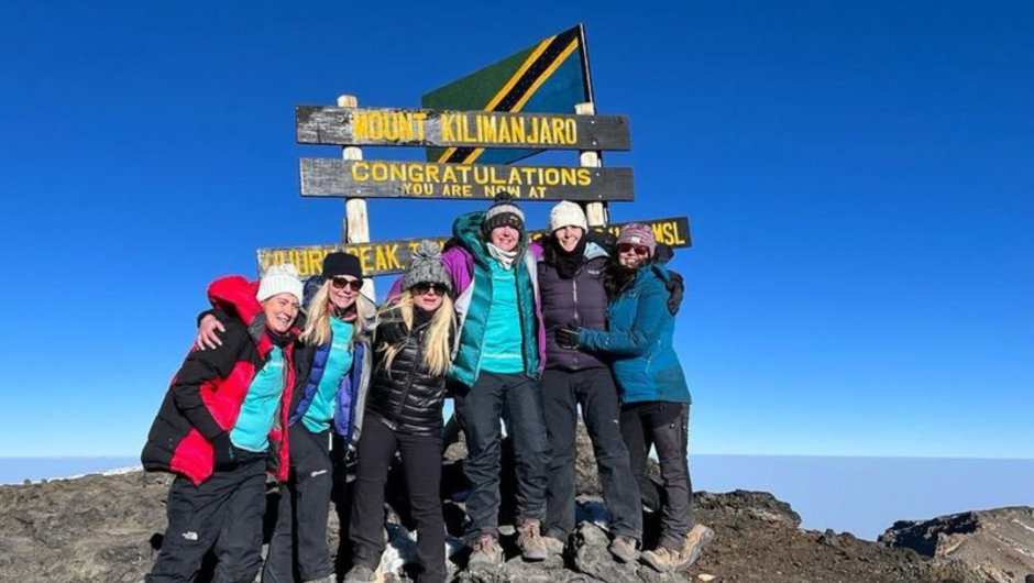 A group of trekkers smiling at the summit of Kilimanjaro in Tanzania.