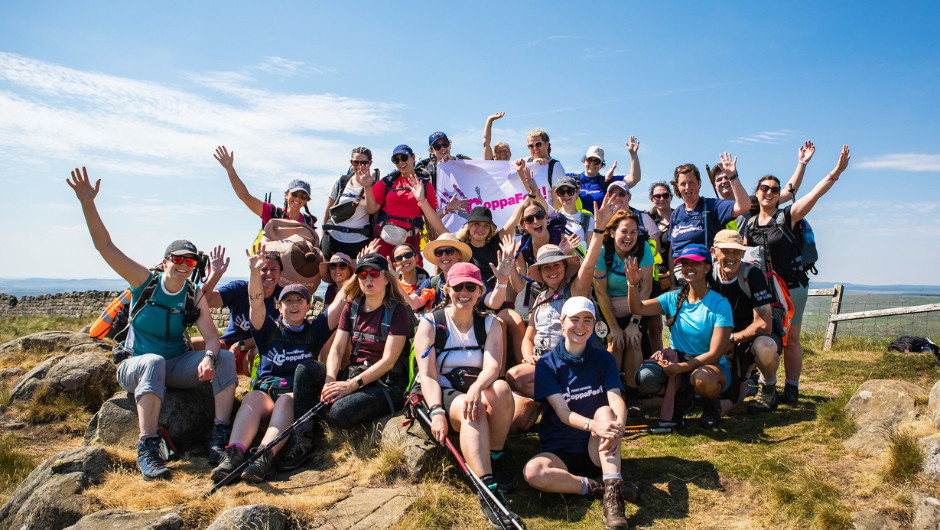 A group of CoppaTrek! hikers celebrating with a Coppafeel flag on a sunny UK trek.