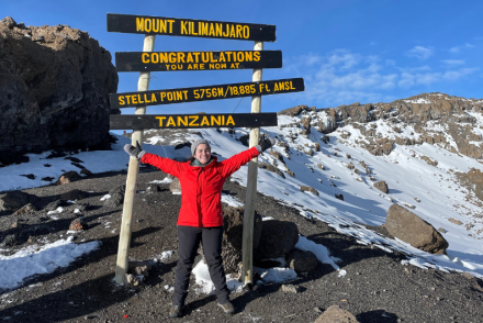 Woman in a red coat celebrating at the Stella Point summit on Mount Kilimanjaro in Tanzania.