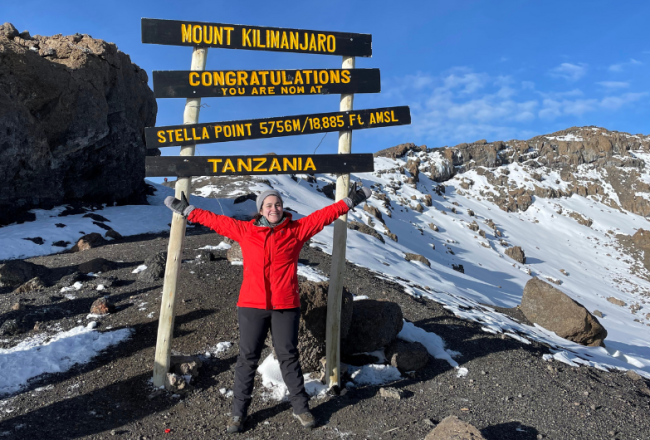 Woman in a red coat celebrating at the Stella Point summit on Mount Kilimanjaro in Tanzania.