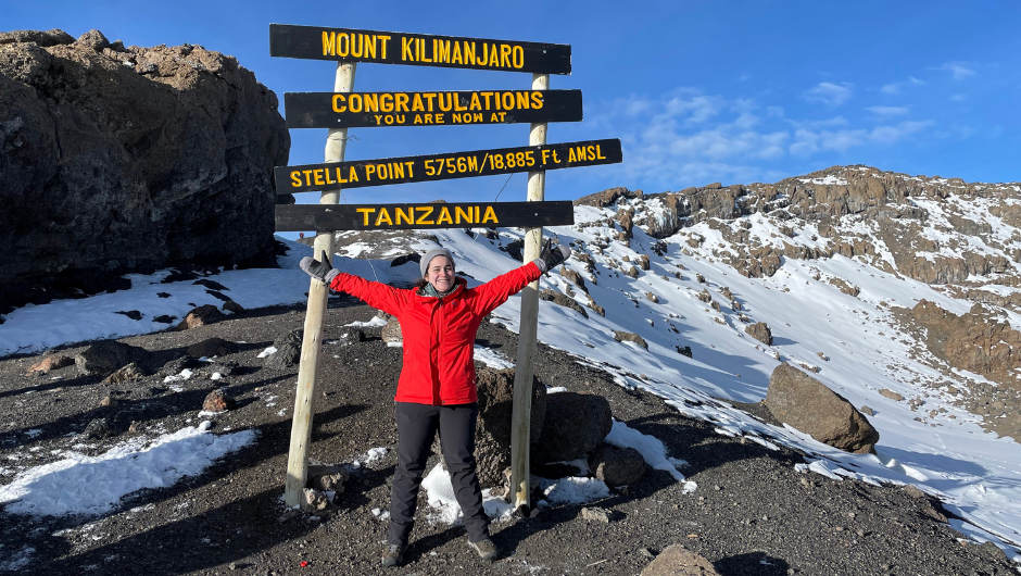 Woman in a red coat celebrating at the Stella Point summit on Mount Kilimanjaro in Tanzania.
