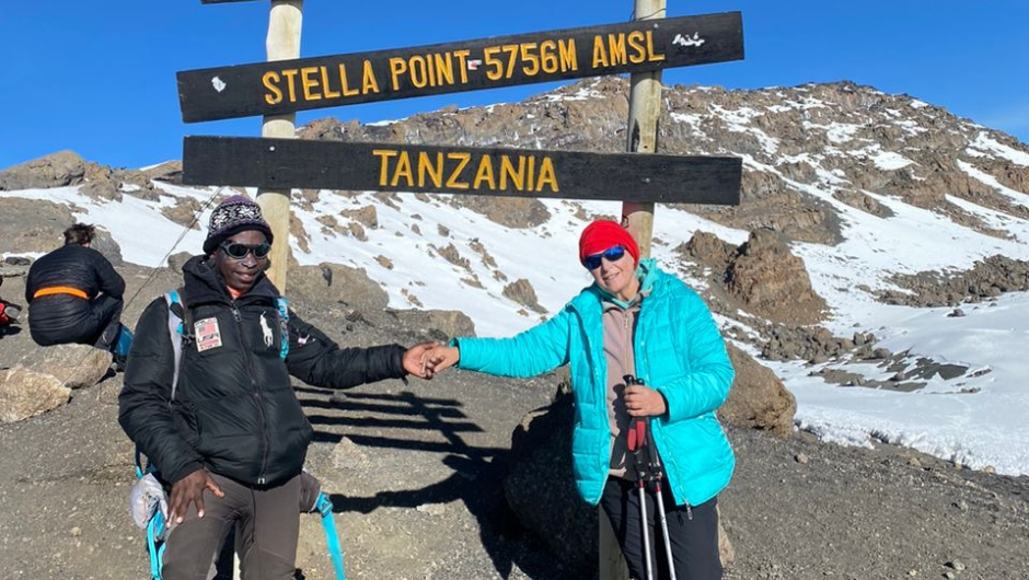 Two hikers holding hands in front of the Mount Kilimanjaro Stella Point sign.