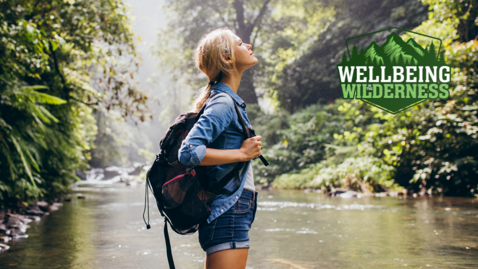A woman standing beside a flowing stream looking up to the sunlight, enjoying the beautiful surroundings of nature