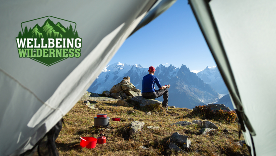 A view looking out of a tent at a trekker sitting on a rock enjoying the view of a snow capped mountain valley in the sunshine