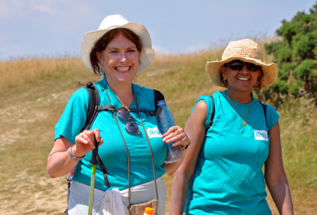 Charity challenge support: from booking to finish line. Two smiling women walking on a sunny south downs challenge