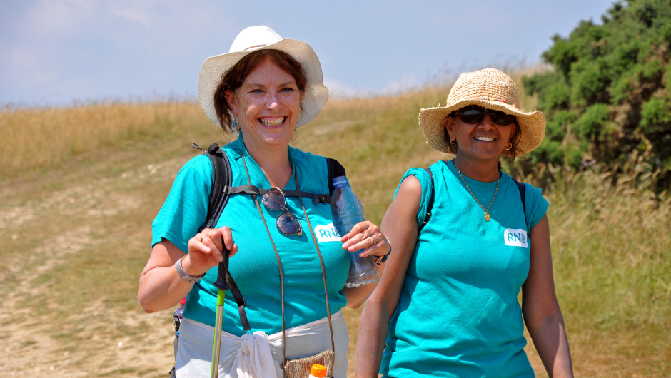 Charity challenge support: from booking to finish line. Two smiling women walking on a sunny south downs challenge