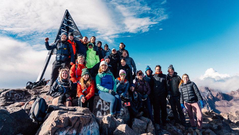 A group of trekkers smiling together at the summit of Mount Toubkal in Morocco.