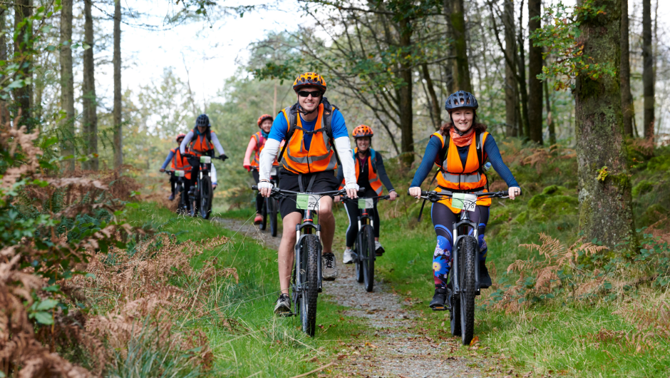 A group of people biking through the Grizedale Forest in the Lake District, wearing helmets and high vis vests.
