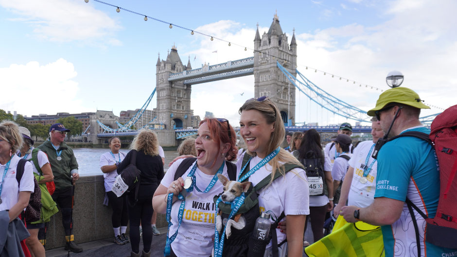 Two people smiling in front of Tower Bridge in London, holding up their Charity Challenge medals, after completing their Thames Footpath Challenge.