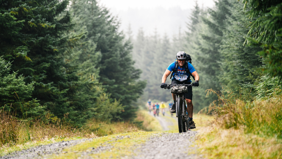 A person riding a mountain bike, cycling over the top of a small hill in Grizedale Forest.