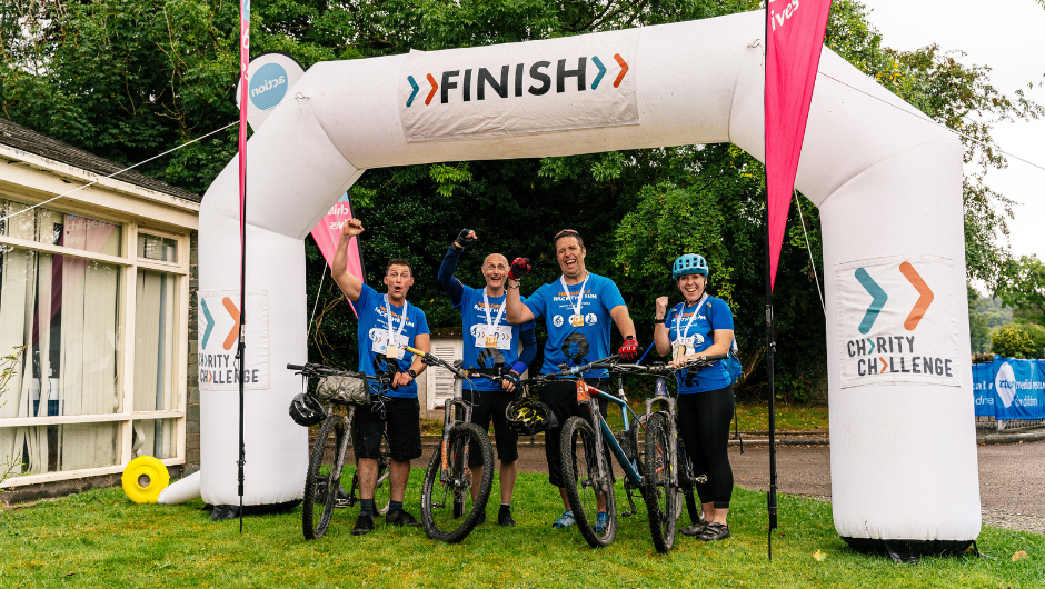 A group of cyclists celebrating at the finish line of their Lake District Triple Challenge.