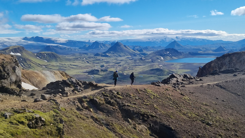 A pair of trekkers walking across a rocky ridge, surrounded by the volcanic peaks and lakes of Iceland.