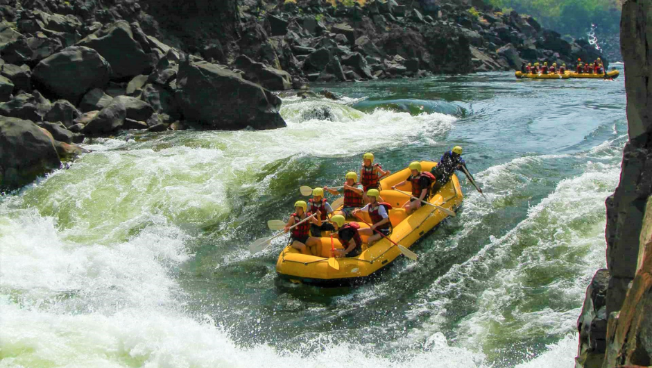 A yellow raft full of people paddling through some white water rapids on the Zambezi River.