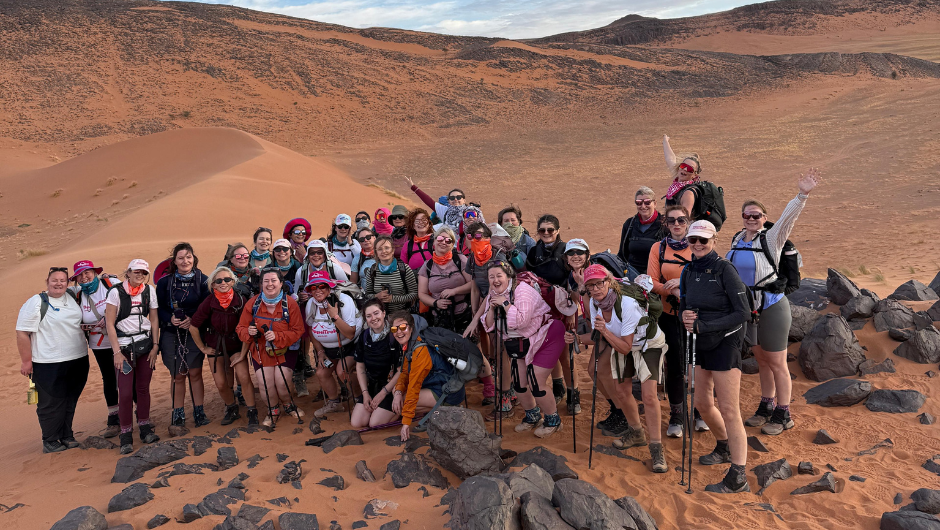 A group of trekkers smiling together in a rocky section of the Sahara Desert, during the CoppaTrek! with Gi Sahara challenge.