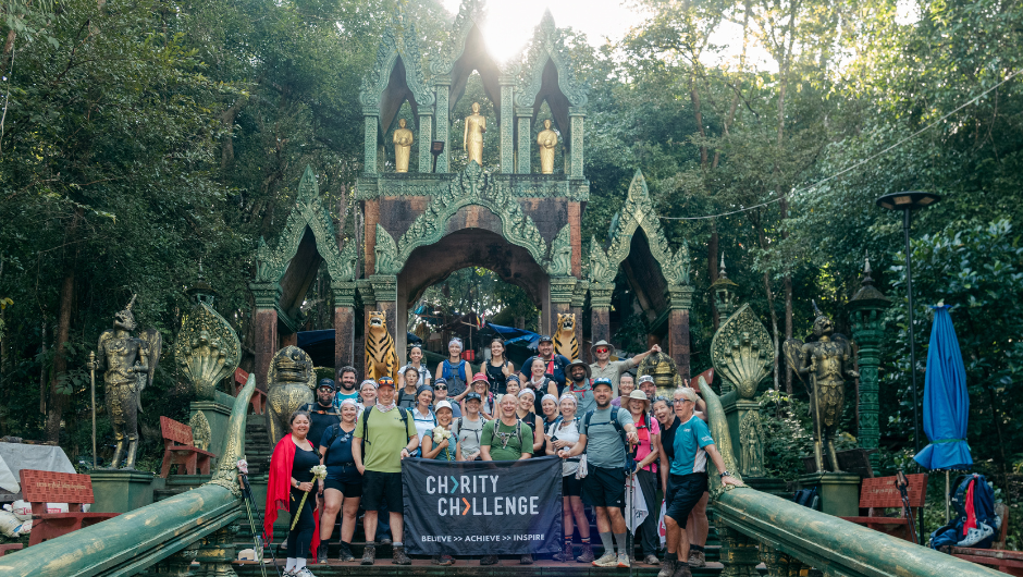 A group of trekkers smiling with a flag that reads 'Charity Challenge' in front of an ancient temple in Cambodia.