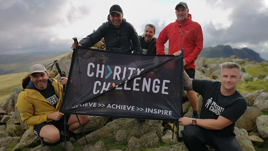 A group of hikers at the summit of a UK mountain holding a Charity Challenge flat up.