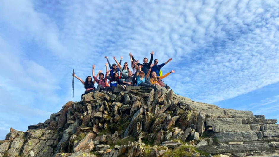 A group of trekkers at the summit of Scafell Pike, cheering with their arms in the air, during their National Three Peaks Challenge.