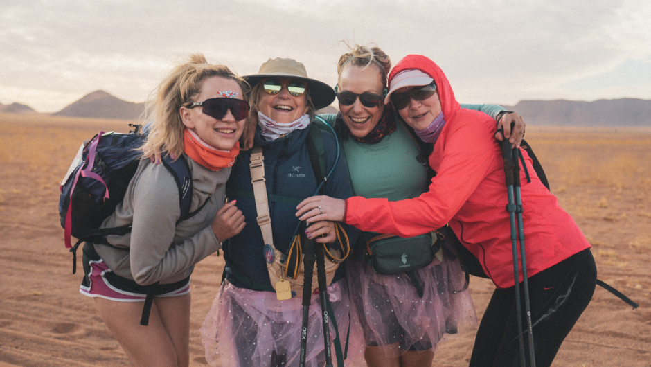 Four trekkers wearing sunglasses and smiling and hugging during their Sahara Desert Trek.