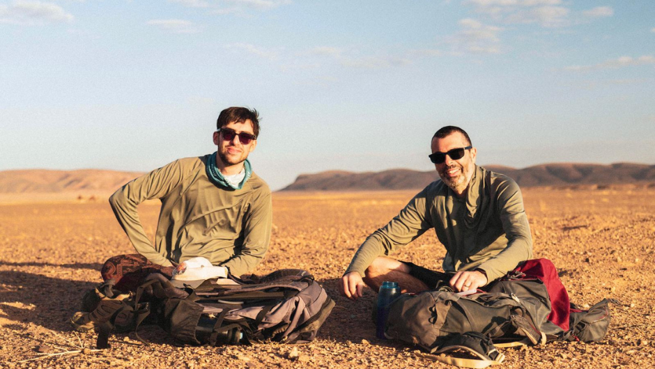 Charity Challenge Director, Simon Albert, sitting and smiling with his son during a Sahara Desert Trek challenge.