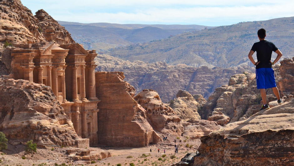 A trekker overlooks Petra’s Monastery from a high vantage point, taking in the vast desert landscape and ancient rock-carved architecture of Jordan.