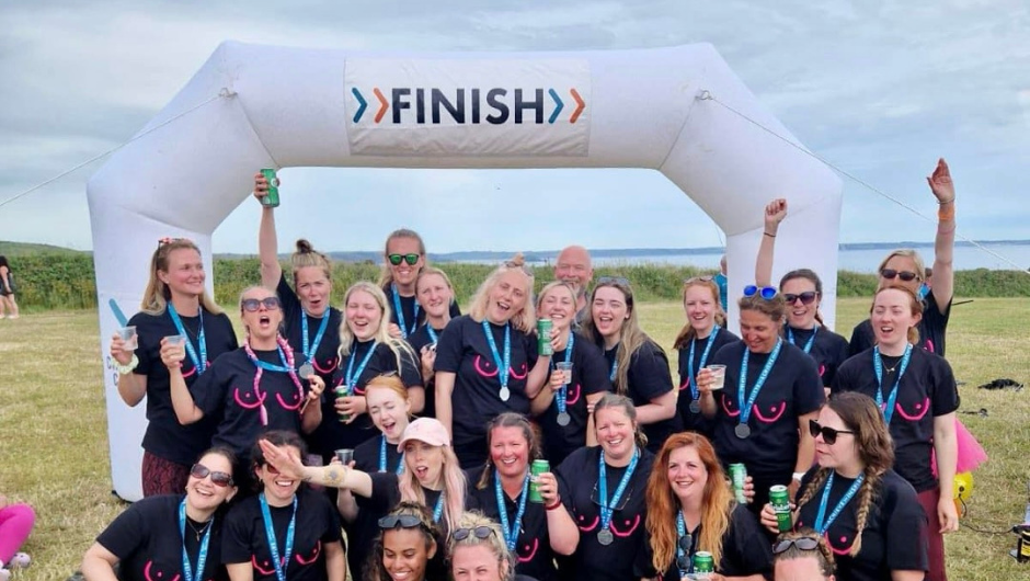 A group of trekkers celebrating in front of a finish line, wearing medals and CoppaFeel! t-shirts.