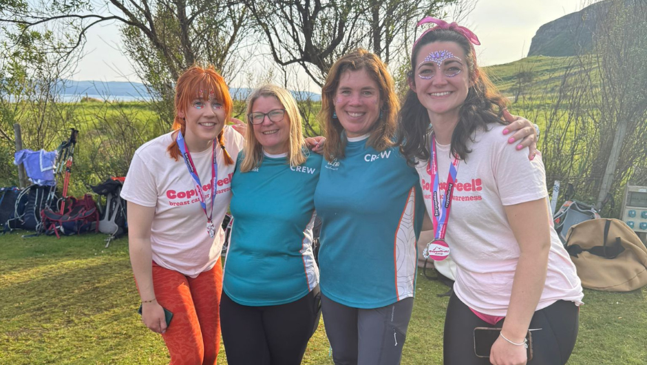 four people, two wearing CoppaFeel! t-shirts and two wearing Charity Challenge crew t-shirts, stood smiling with their arms around each other at a UK campsite.