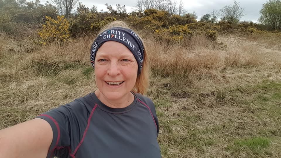 a challenge leader wearing a charity challenge neck buff as a headband whilst out on a walk in a grassy field