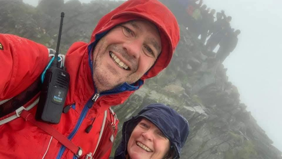 two challenge leaders wearing rain coats smiling for a selfie at the top of a rainy scafell pike
