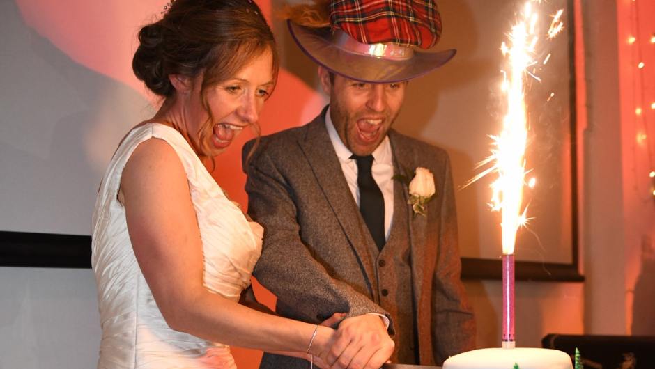 Two people smiling as they cut their wedding cake together.