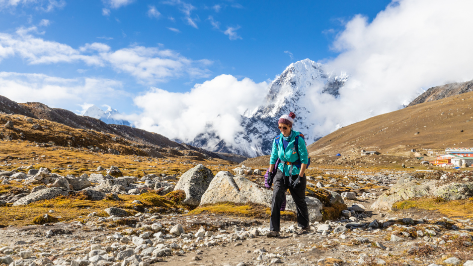 A trekker dressed in warm layers walking along a rocky section of the Everest Base Camp trek.