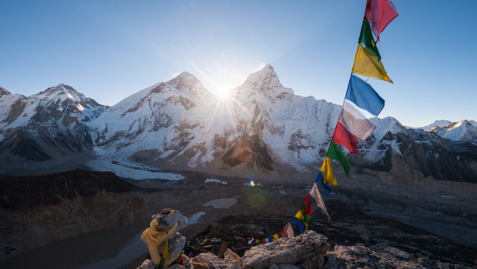 Sunrise over snow-covered Himalayan peaks, with colourful prayer flags fluttering in the foreground.
