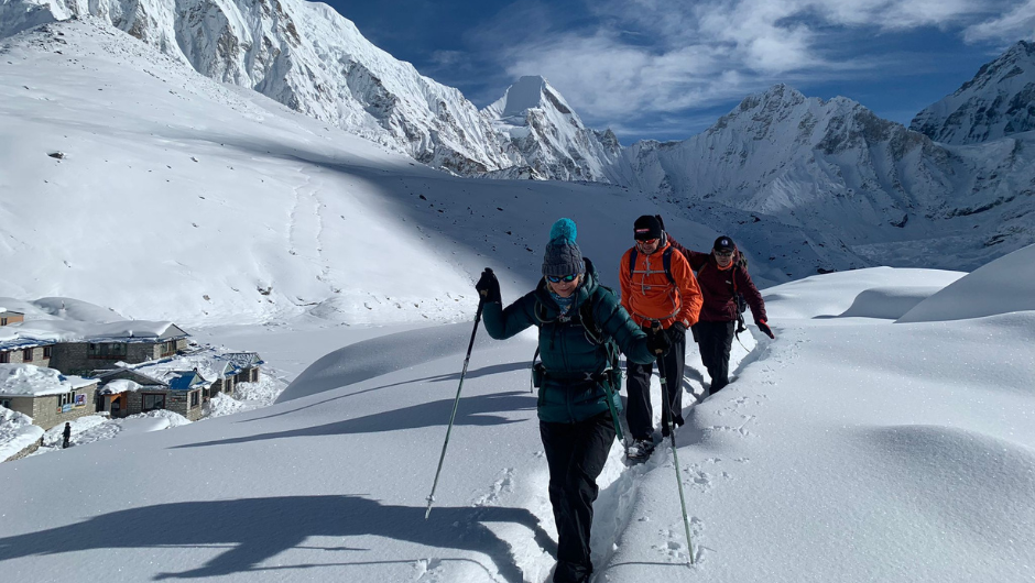 Three trekkers dressed in warm layers walking through a snowy section of the trek to Everest Base Camp.