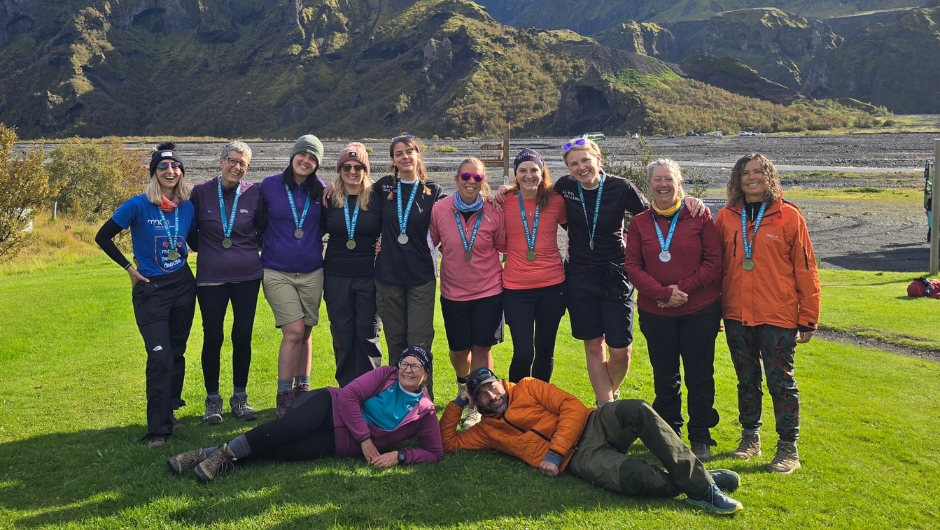 a group of icelandic lava trek challengers stood together in front of rugged icelandic rocks, smiling and wearing Charity Challenge medals