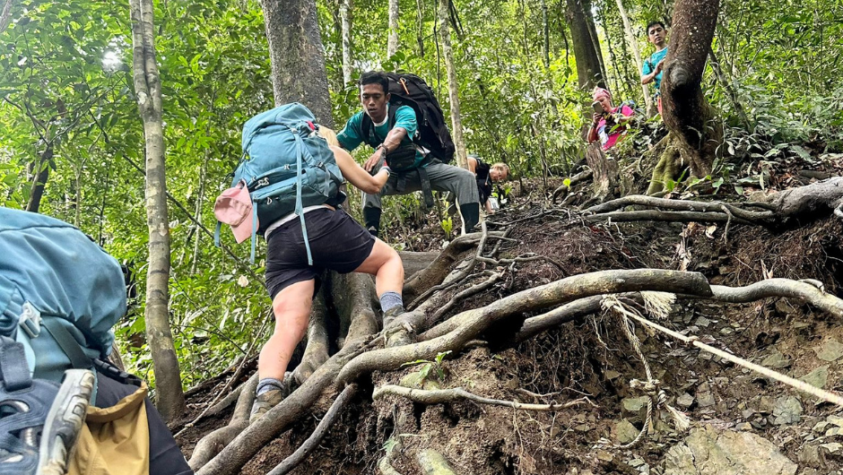 A Charity Challenge Guide helping a trekker up a steep section of the Sumatra Jungle.