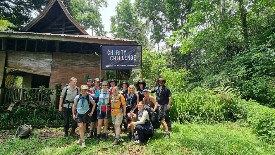 A group of trekkers in the Sumatra Jungle in Indonesia, wearing Charity Challenge medals, stood under a Charity Challenge flag.