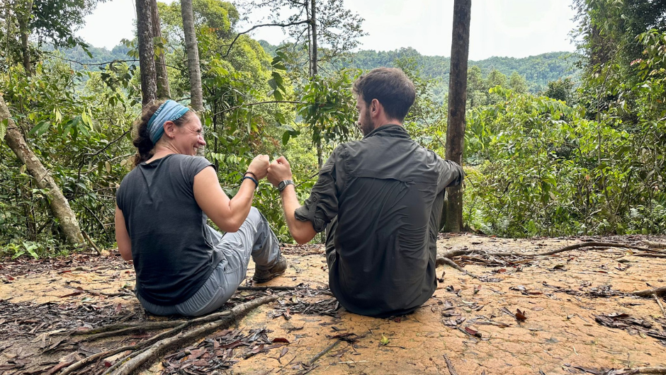A Charity Challenge leader and participant 'fist bumping' as they sit and look at views of the lush Sumatran Rainforest.