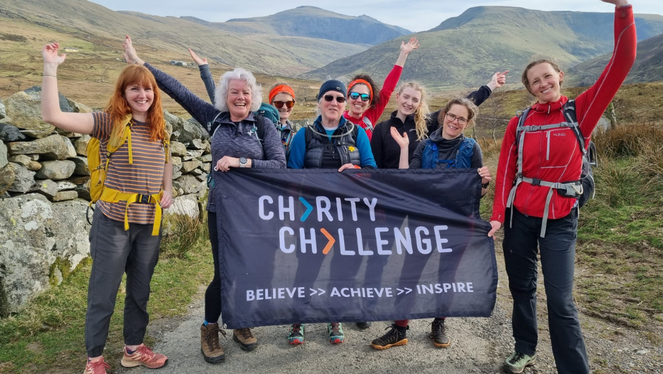 A group of female mountain leaders smiling together whilst holding a Charity Challenge banner.