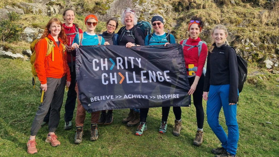A group of female mountain leaders smiling together and holding a Charity Challenge banner.