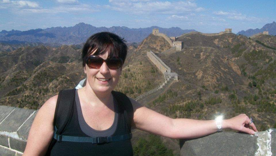 A smiling woman wearing sunglasses and a trekking daypack on a section of the Great Wall of China.
